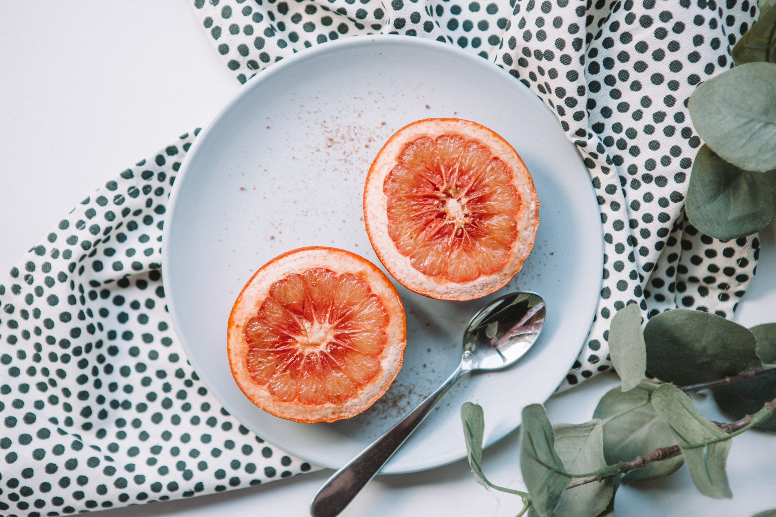 two halves of grapefruit on white plate with spoon - foods for fertility